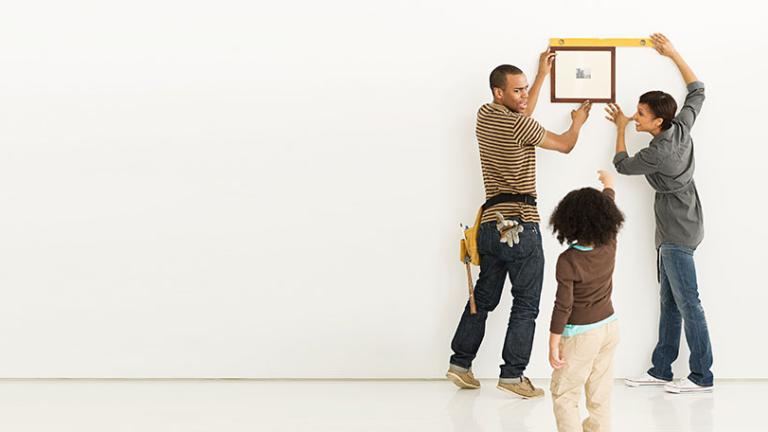 Two adults and a child hanging a picture frame